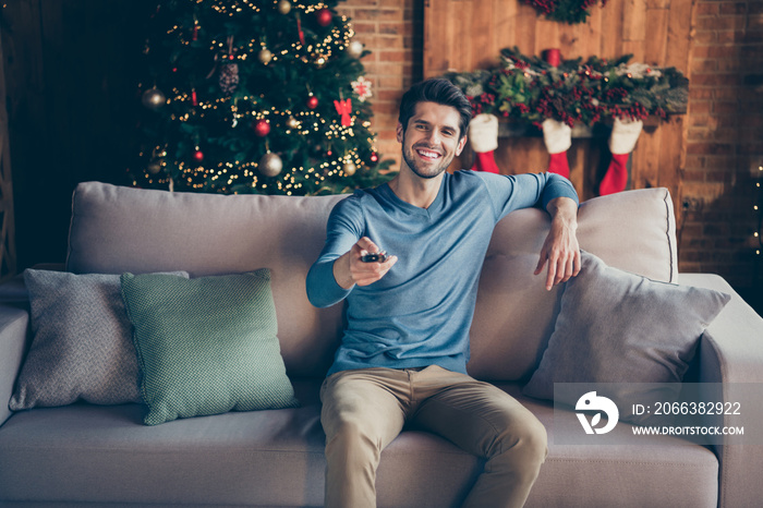 Portrait of positive guy sit couch watch tv christmas films switch channels enjoy newyear atmosphere