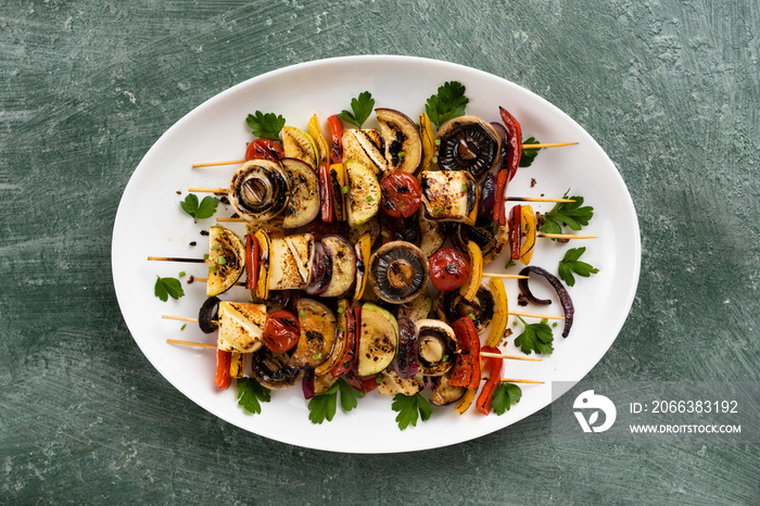 Vegetarian barbecue vegetable skewers with tofu cheese in a white dish on the table, food outdoors