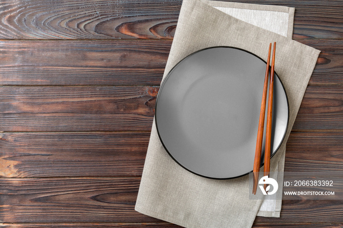 Empty grey round plate with chopsticks for sushi and soy sauce on wooden background. Top view with c