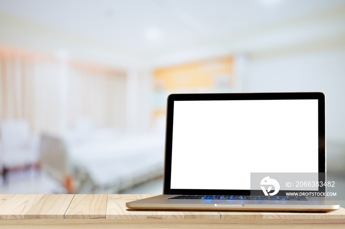 Laptop on wood desk at hospital room with bed  background.  Blank screen For Graphic display montage