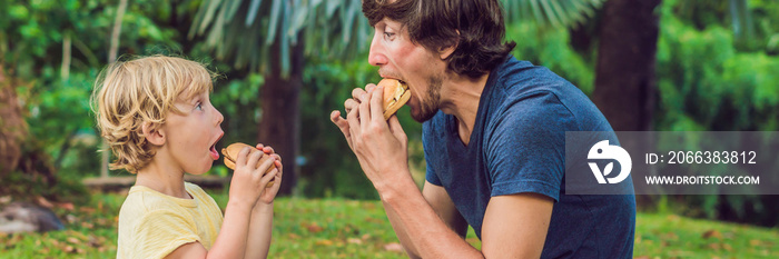 Portrait of a young father and his son enjoying a hamburger in a park and smiling BANNER long format