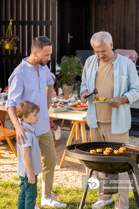 Mature man, his son and grandson making grilled corn for family dinner on weekend