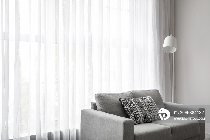 Interior of light living room with grey sofa, standard lamp and curtain