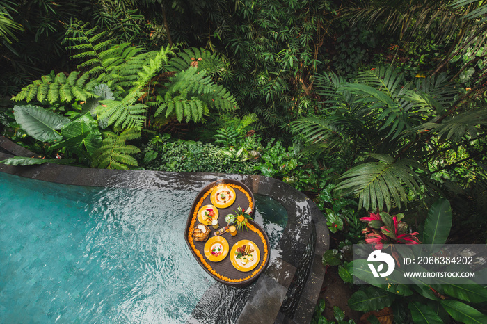 Floating breakfast in jungle swimming pool, tropical resort. Black rattan tray in heart shape, Valen