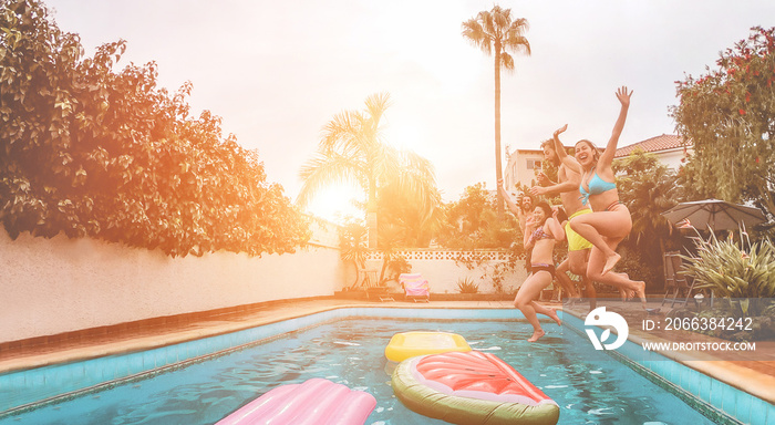 Happy friends drinking jumping in swimming pool at sunset - Young  people having fun in tropical vac