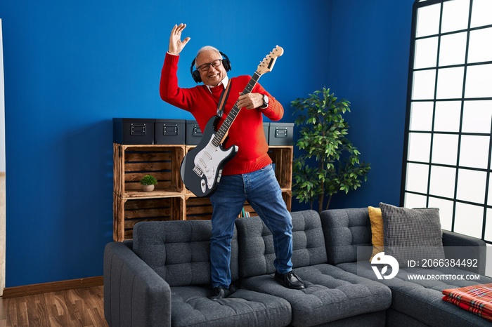 Senior man playing electrical guitar standing on sofa at home