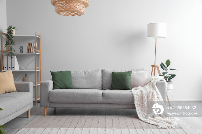 Grey sofa with cushions and plaid in interior of light living room