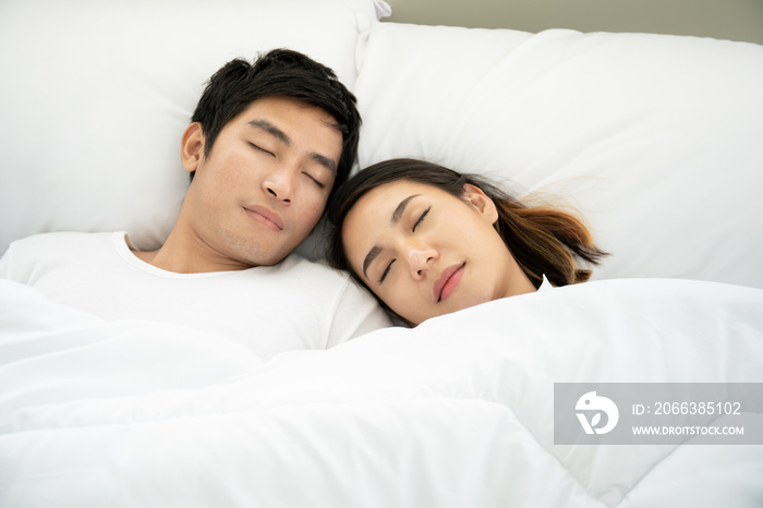 Young Asian couple sleeping on the white bed together close up.