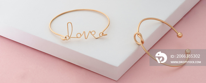 Word love and knot shape golden bracelets on pink and white background