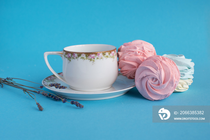 Homemade pink zephyr or marshmallow with white porcelain cup and lavander close to. Isolated on blue