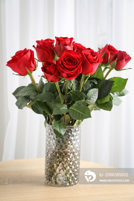 Vase with bouquet of red roses on wooden table, space for text