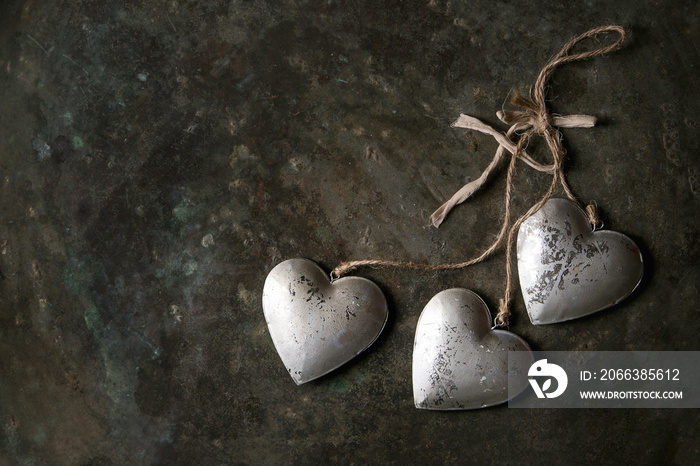 Love Valentines day greeting card with three silver hearts on rope cord over old dark metal backgrou