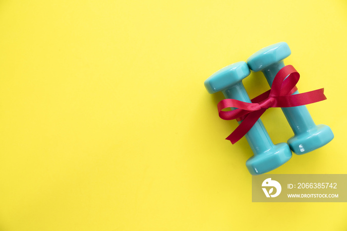 two green dumbbell with red gift bow on a yellow table background, sport and healthy concep