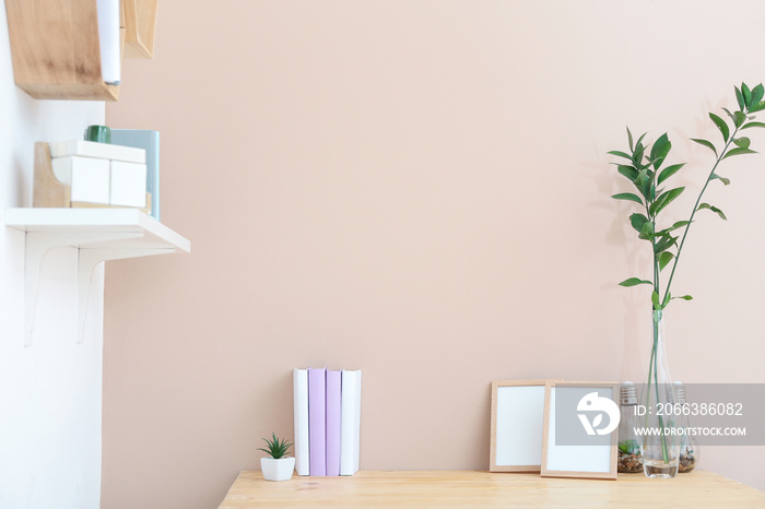 Books, frames and floral decor on table near color wall