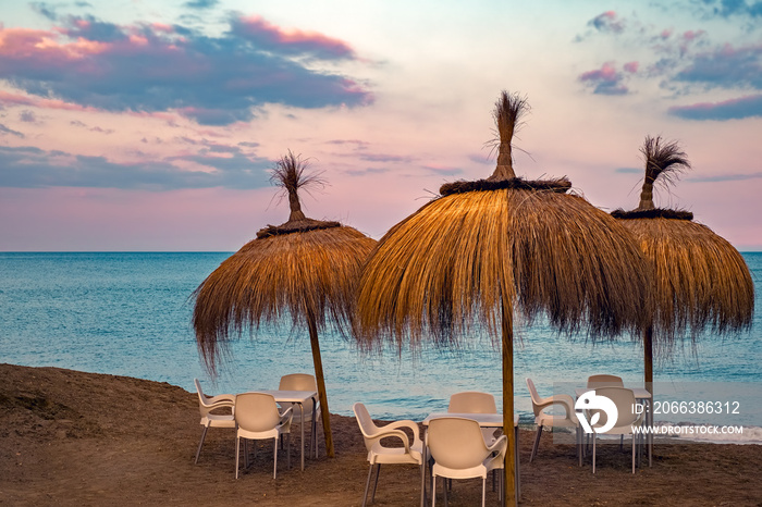 empty table and chairs with straw umbrella on the beach. at the sunset