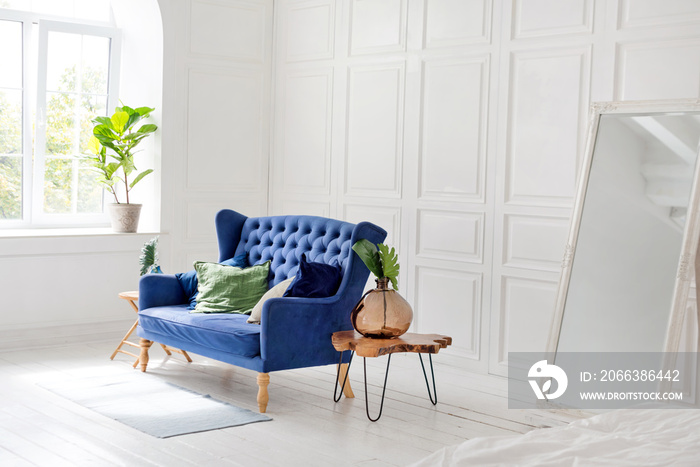 Comfortable classic blue couch with pillows and wooden coffee table in simple white apartment