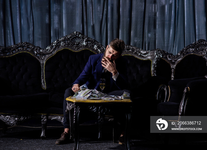 Millionaire in elegant suit smokes and drinks on luxurious sofa.