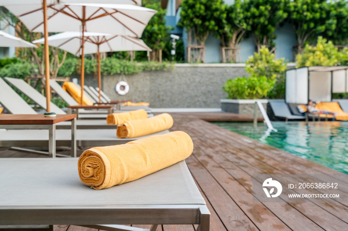 Rolled up orange towel on a sun lounger background of pool in resort or hotel.