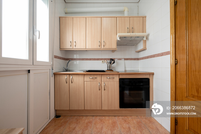 Wall of an apartment kitchen covered in wood-colored furniture with a black oven, a white aluminum w