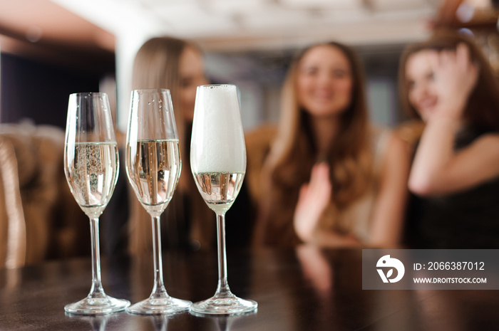 Man fills glasses of champagne for three beautiful young women in restaurant