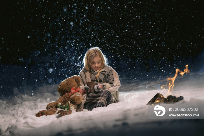 cute little girl sitting and warming herself by the fire in the winter evening. fantastic night by t