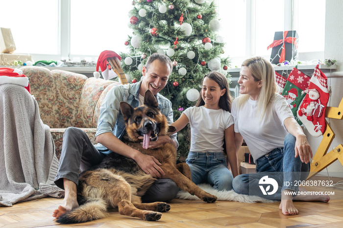 Excited girl and her family sitting on the floor near christmas tree and smiling. family during Chri