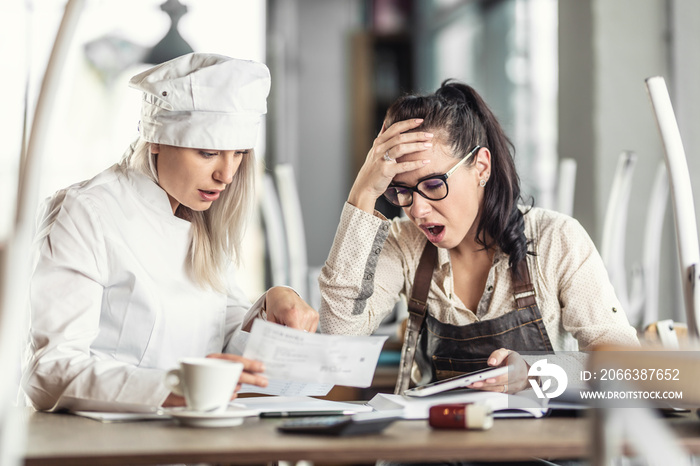 Shock over bookkeeping by female chef and restaurant owner, sitting over paperwork