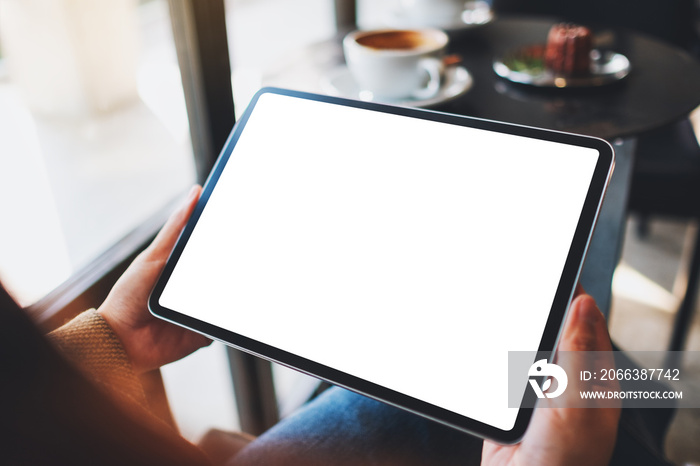 Mockup image of a woman holding black tablet pc with blank white screen in cafe