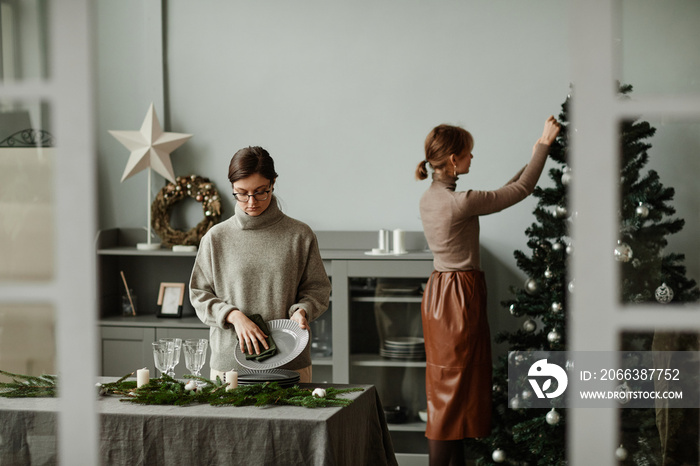 Portrait of two young women setting up dining room decorated for Christmas with fir branches and can