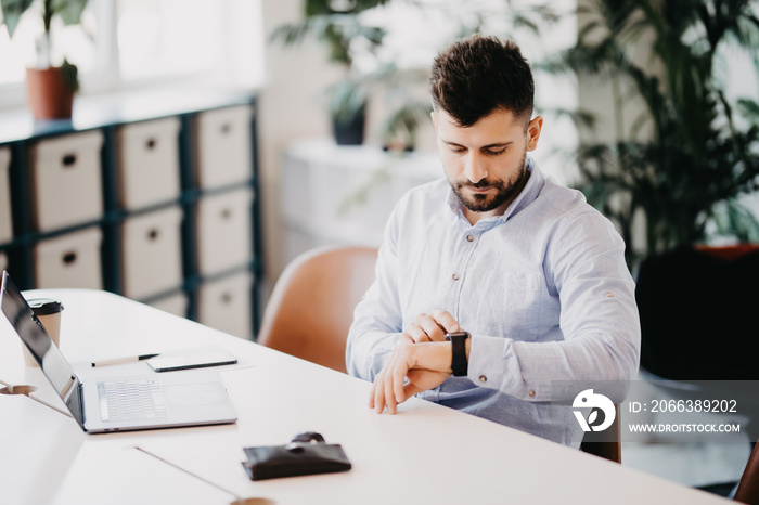 Modern innovations. Handsome young man setting smart watch while sitting at the desk in creative off