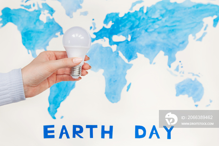 Energy saving light bulb in human hand on world map background with text Earth day. Concept ecology,