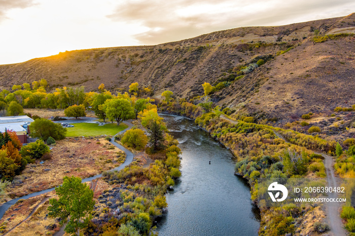 Aerial view of a beautiful River in Autumn with colorful trees, barren desert mountains, and a partly cloudy blue sky near Reno Nevada.