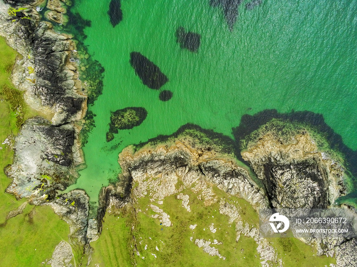 West coast of Ireland. Aerial drone top down view. Green fields and rocky shore. Rocks under water make foot print shape or exclamation mark.