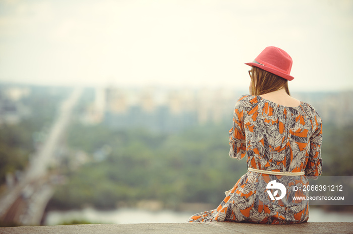 girl in a dress and hat looks at the city from a height