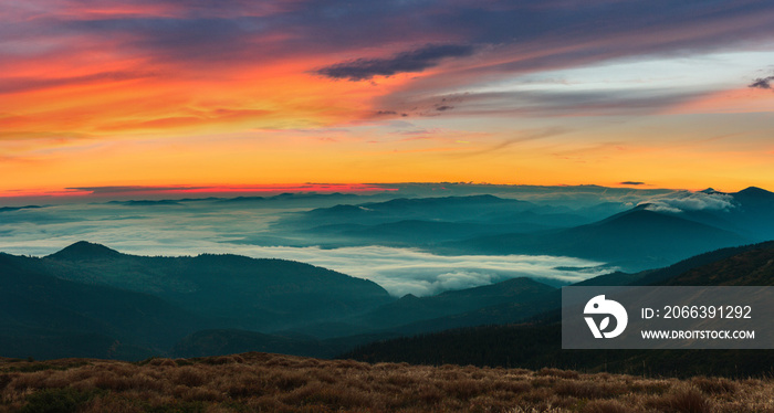 Amazing panoramic landscape in the mountains at sunrise. View of colorful sky and foggy hills covered by forest. Concept of the awakening wildlife.