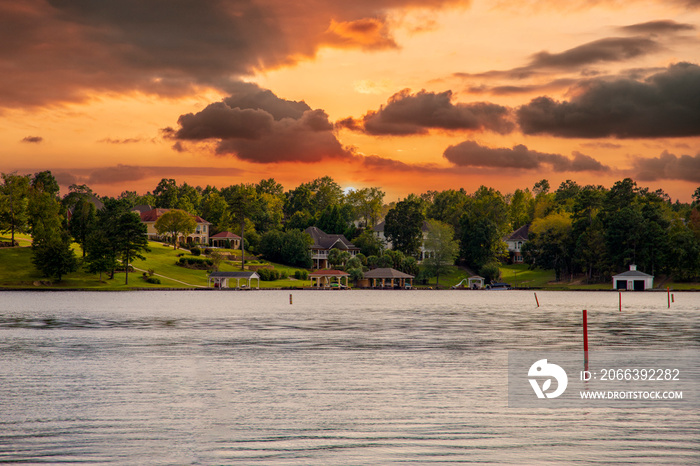 a gorgeous autumn landscape on Lake Tobesofkee with lakefront homes along the banks surrounded by lush green trees, grass and plants with powerful clouds at sunset in Lizella Georgia USA