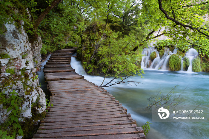 Beautiful view of waterfalls with turquoise water and wooden pathway through over water. Plitvice Lakes National Park, Croatia. Famous attraction, summer landscape.