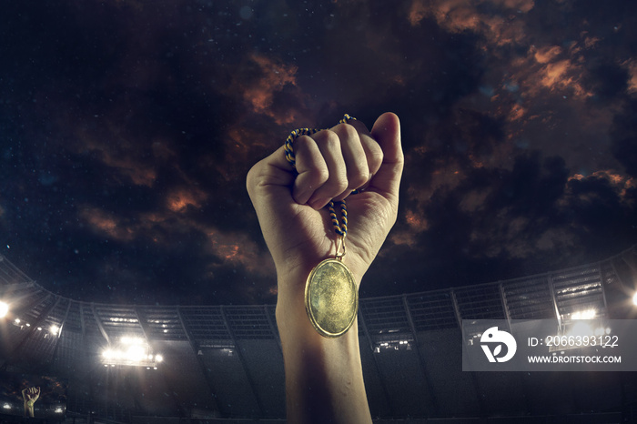 Champion. Award of victory, male hands tightening the golden medal of winners against cloudy dark sky. Sport, competition, championship, winning, achieving the goal. Prize for success and honor.