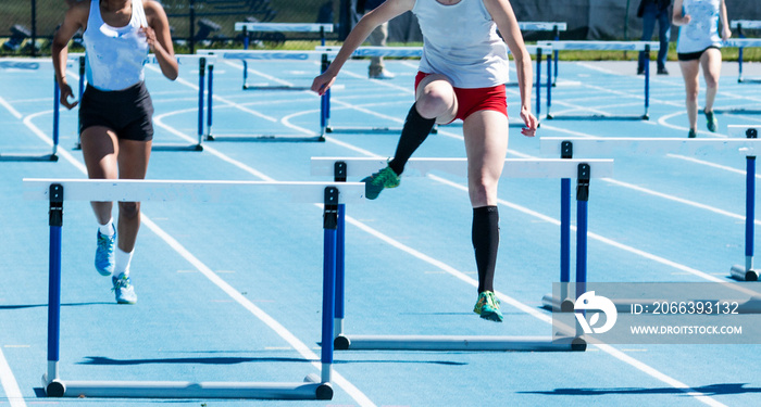 Girls running in a hurdle race on a blue track