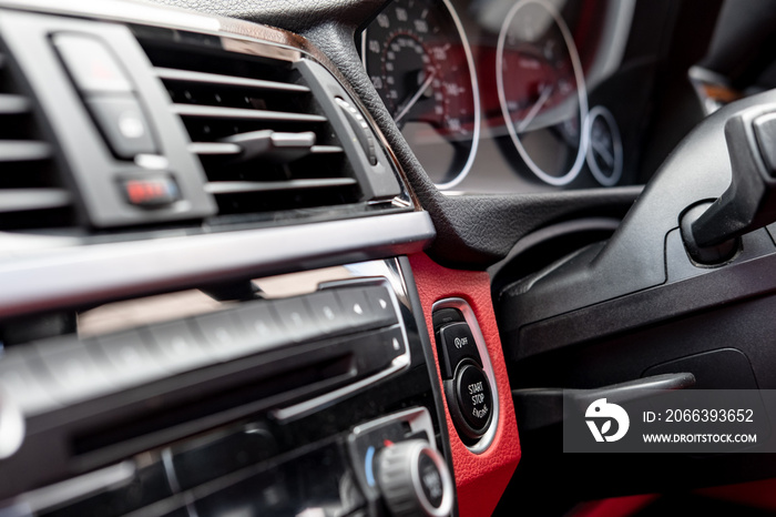 Shallow focus image of an engine Start Stop button seen on the dashboard of a luxury, german made sports car. Some of the radio, air-con and dials are visible