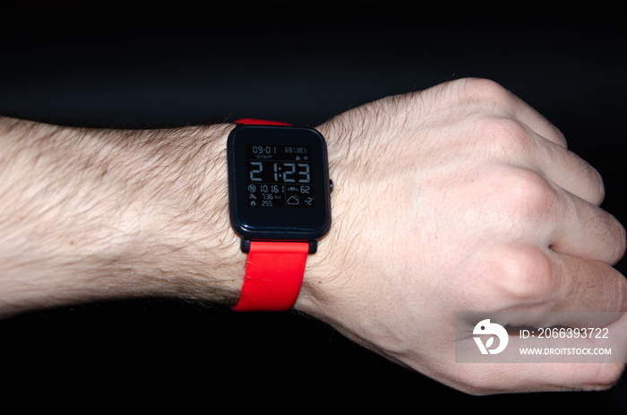 Smart watch with a red strap. Smart watch with a bright strap on his hand and on a black background. Tracking sports activity. Playing sports