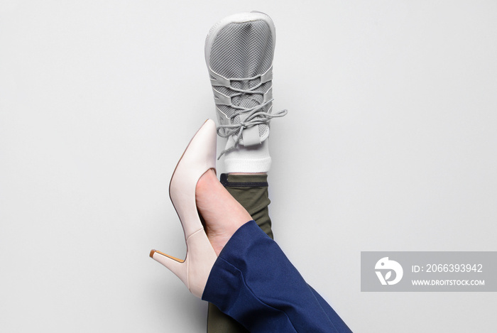 Legs of woman in sports and high-heeled shoes on light background