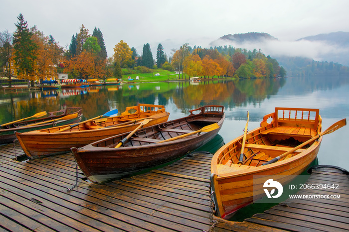 Autumn scenery with boats moored on Bled lake at foggy day