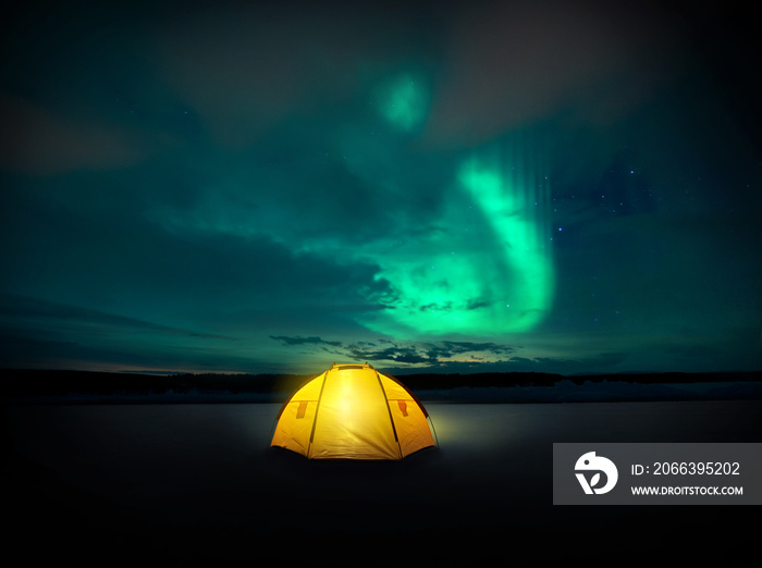 Out in the wilderness The Norther lights ( Aurora Borealis) dances across the night sky in Sweden, above the glowing lights from the camping tent. Photo Composite.