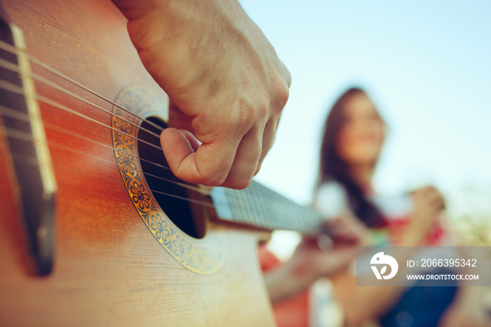 Couple sitting and resting on the beach playing guitar on a summer day near river