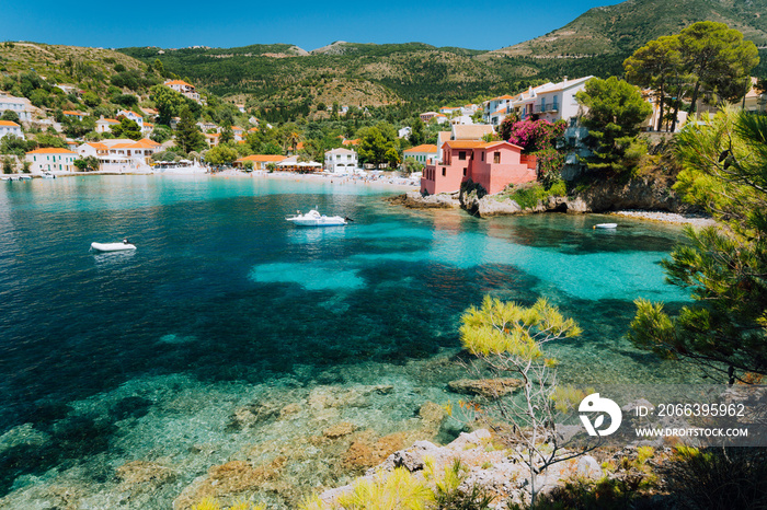 Assos village, Kefalonia Greece. View to cute bay with vivid colored houses and transparent turquoise water surrounded by green pine trees. Blue deep pattern on bottom