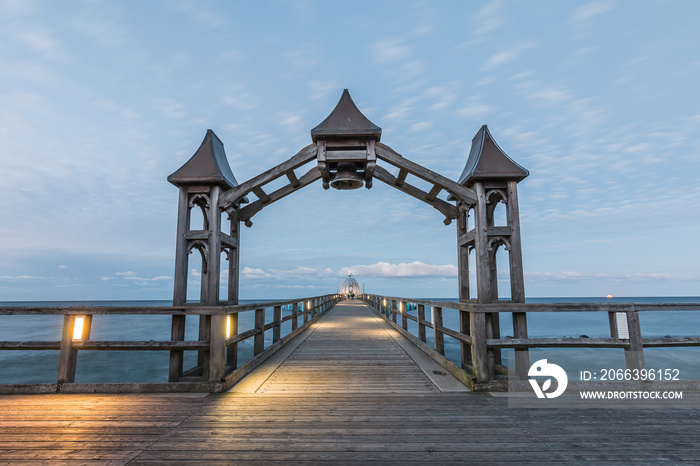 Wooden pier on the Baltic Sea. View to the horizon with sunset and clouds. Illuminated jetty with wooden arch and diving bell in the background on the island of Ruegen