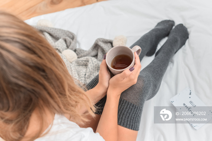 Woman`s legs in leg warmers in bed. Beautiful girl sitting in her bed and drinking morning tea