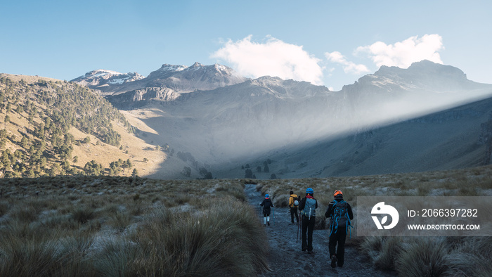 Group of hikers walking in grassland with mountains in the background. Iztaccihuatl