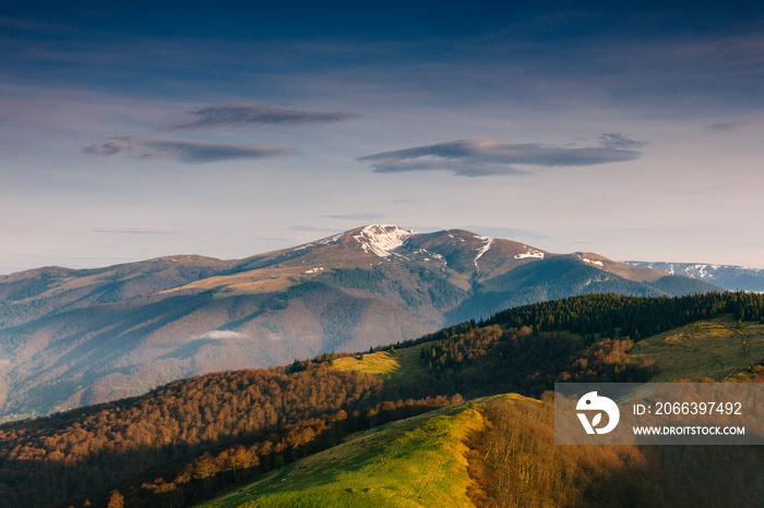 Beautiful mountains landscape in spring. Springtime in mountains.  View of forested hills and grassy slopes illuminated with sunshine. Dramatic sky. Wild scenery. Europe.